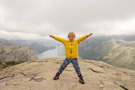 Photo for Family, enjoying the hike to Preikestolen, the Pulpit Rock in Lysebotn, Norway on a rainy day, toddler climbing with his pet dog the one of the most scenic fjords in Norway - Royalty Free Image