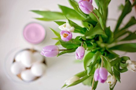 Téléchargez les photos : Beau vase avec des tulipes blanches et violettes sur une table avec des bougies et des œufs de Pâques, floue en arrière-plan - en image libre de droit