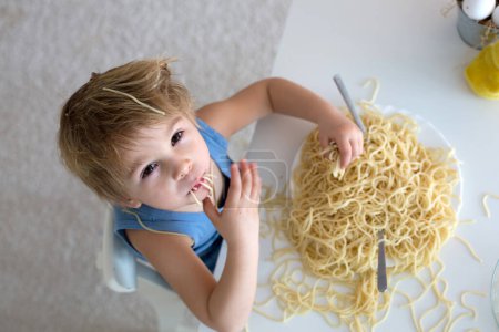 Photo for Little blond boy, toddler child, eating spaghetti for lunch and making a mess at home in kitchen - Royalty Free Image