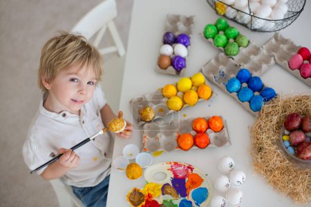 Photo for Beautiful blond child, toddler boy, painting easter eggs with mother at home, making easter wreath with rainbow colors - Royalty Free Image