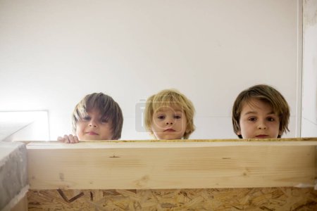 Photo for Three children, boy brothers, lying down in a narrow gap over the doors at home - Royalty Free Image