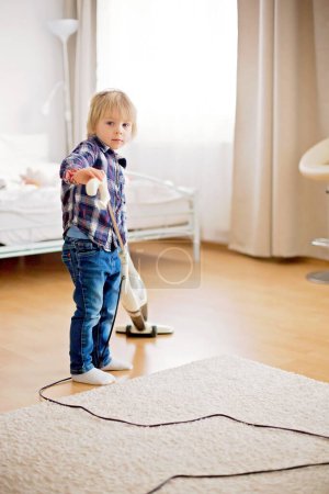 Foto de Lindo niño pequeño, niño, limpieza al vacío en la sala de estar en casa - Imagen libre de derechos