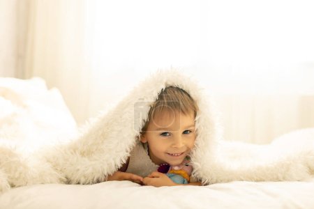 Foto de Pequeño niño pequeño, lindo niño con un juguete de punto pequeño y lindo animal, acostado en la cama, abrazándose - Imagen libre de derechos