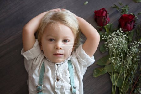 Téléchargez les photos : Beau petit garçon, tenant des roses rouges comme cadeau pour la fête des mères - en image libre de droit