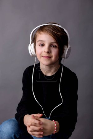 Téléchargez les photos : Enfant doux, garçon en pull noir, écouter de la musique, fond isolé - en image libre de droit