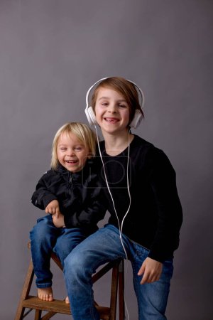 Téléchargez les photos : Enfants doux, garçons frères en chandails noirs, écouter de la musique, fond isolé - en image libre de droit