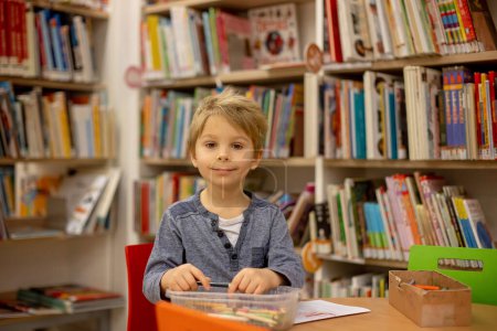 Photo for Adorable little child, boy, sitting in library, reading book and choosing what to lend, kid in book store - Royalty Free Image