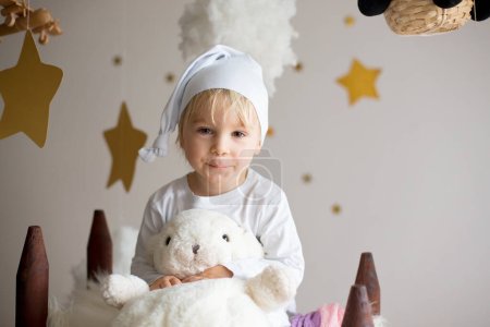 Téléchargez les photos : Enfant mignon, garçon blond, jouant la nuit avec une écharpe colorée et un ours en peluche - en image libre de droit