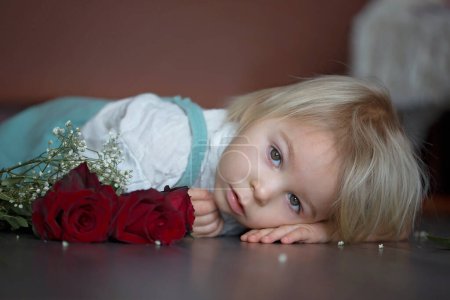 Foto de Hermoso niño, sosteniendo rosas rojas como regalo para el día de la madre - Imagen libre de derechos