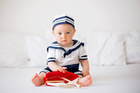 Téléchargez les photos : Bébé garçon mignon, vêtu de vêtements marins, jouant avec un bateau en bois - en image libre de droit