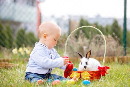 Téléchargez les photos : Doux petit garçon chassant pour l'oeuf de Pâques dans le parc de printemps le jour de Pâques. Mignon petit enfant avec adorable lapin mignon célébrant fête en plein air - en image libre de droit