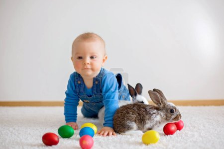 Téléchargez les photos : Petit enfant en bas âge, bébé garçon, jouer avec des lapins et des œufs de Pâques à la maison, dessins colorés à la main sur les œufs - en image libre de droit