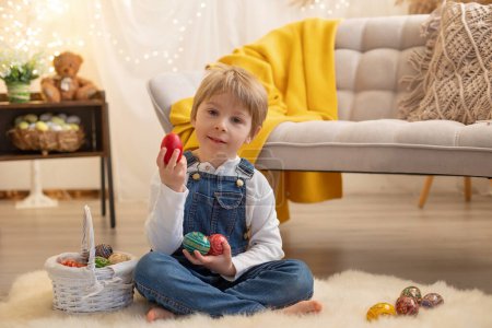Téléchargez les photos : Doux garçon d'âge préscolaire en studio, jouant avec, oeuf pour Pâques et manger du chocolat, enfant en vacances de Pâques à la maison - en image libre de droit