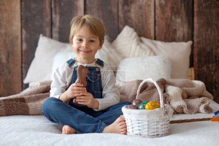 Foto de Dulce niño preescolar en el estudio, jugando con, huevo para Pascua y comer chocolate, niño en vacaciones de Pascua en casa - Imagen libre de derechos