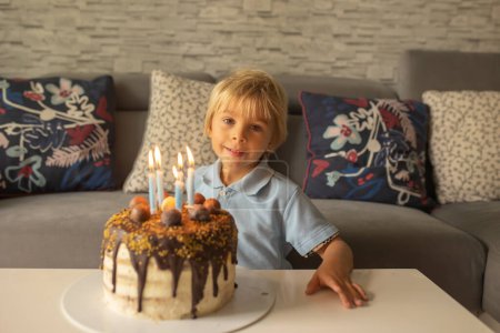 Foto de Hermoso adorable niño de cinco años en camisa azul, celebrando su cumpleaños con pastel casero - Imagen libre de derechos