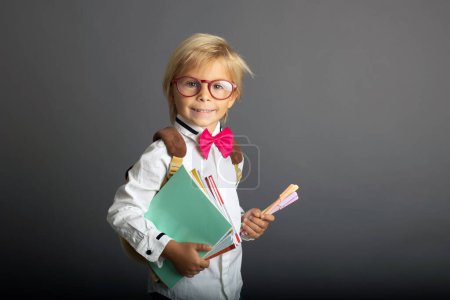 Téléchargez les photos : Cute preschool blond child, boy, holding books and notebook, apple, wearing glasses, ready to go to school - en image libre de droit