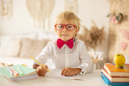 Foto de Cute preschool blond child, boy, holding books and notebook, apple, wearing glasses, ready to go to school - Imagen libre de derechos