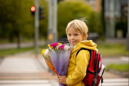 Téléchargez les photos : Mignon enfant d'âge préscolaire, en attente d'un feu rouge pour traverser la rue, des bouquets de fleurs pour les enseignants, aller à l'école maternelle, premier jour à l'école - en image libre de droit