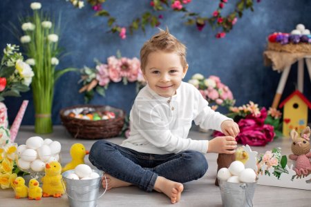 Téléchargez les photos : Enfant tout-petit élégant et mignon, garçon avec chemise blanche, jouant avec des œufs et un lapin en chocolat sur la décoration de Pâques, plan studio - en image libre de droit