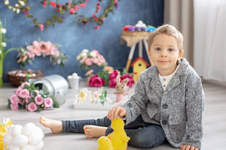 Foto de Lindo niño pequeño con estilo, niño con camisa blanca, jugando con huevos y conejito de chocolate en la decoración de Pascua, tiro al estudio - Imagen libre de derechos