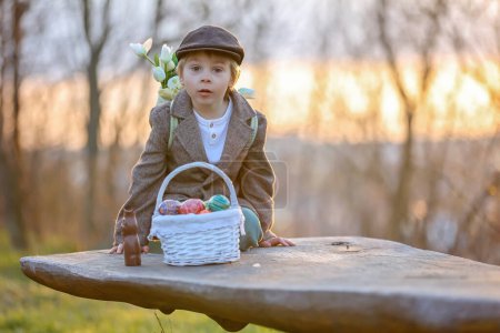 Foto de Hermoso niño pequeño con estilo, niño, jugando con la decoración de Pascua en el parque, primavera al atardecer - Imagen libre de derechos