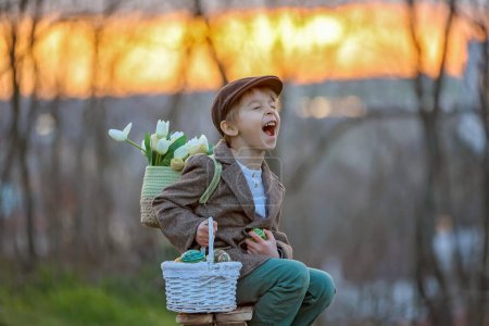 Téléchargez les photos : Beau tout-petit élégant enfant, garçon, jouer avec la décoration de Pâques dans le parc, printemps au coucher du soleil - en image libre de droit