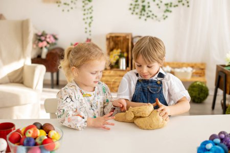 Téléchargez les photos : Petit garçon blond tout-petit avec sœur, préparant de la pâte pour des brioches de Pâques, du pain de Pâques sucré aux noix et aux fruits secs à la maison - en image libre de droit