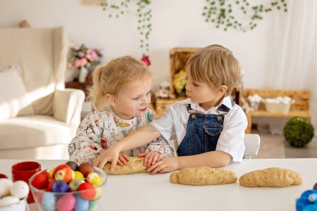 Foto de Pequeño niño rubio niño con hermana, preparando masa para panecillos de brioche de Pascua, pan dulce de Pascua con nueces y frutas secas en casa - Imagen libre de derechos
