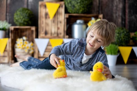 Foto de Lindo niño preescolar joven, niño, jugando con patos en casa, hermosa decoración de primavera para el cumpleaños detrás de él - Imagen libre de derechos