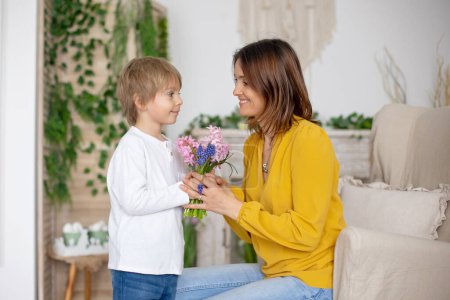 Photo for Cute little boy, giving flowers to his mom for Mothers day at home, cozy place - Royalty Free Image
