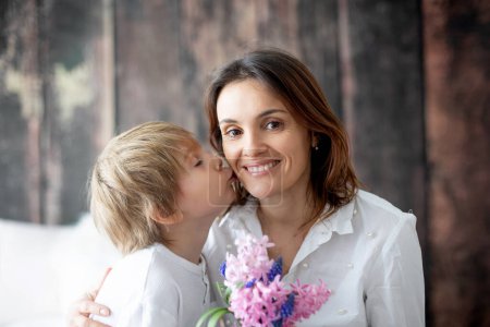 Téléchargez les photos : Petit garçon mignon, donnant des fleurs à sa mère pour la fête des mères à la maison, endroit confortable - en image libre de droit
