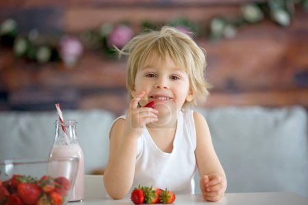 Téléchargez les photos : Enfant tout-petit mignon, garçon blond, boire du smoothie et des fraises de Pâques à la maison - en image libre de droit