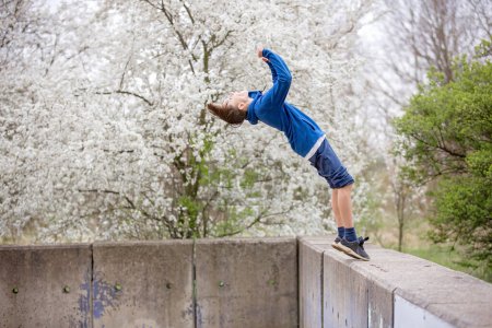 Photo for Teen child, boy, making summersaults in the park, springtime - Royalty Free Image