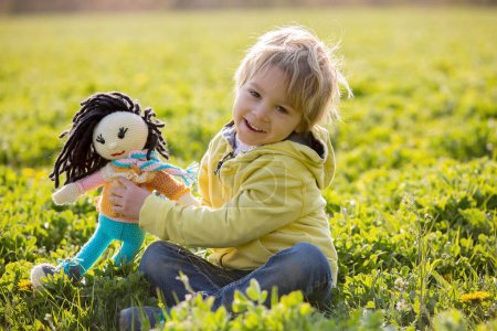 Téléchargez les photos : Petit tout-petit blond enfant, garçon, jouer avec une poupée tricotée à la main dans le parc - en image libre de droit