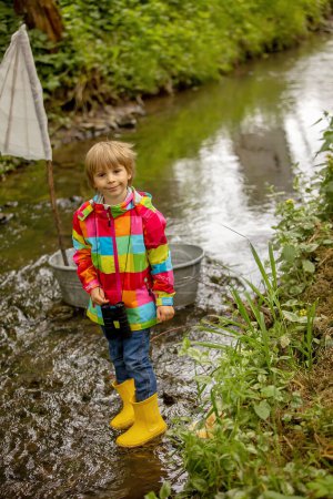 Foto de Lindo niño, niño con chaqueta de colores, jugando con el barco y patos en un pequeño río, vela y paseos en bote. Niño divertirse, concepto de felicidad de la infancia - Imagen libre de derechos