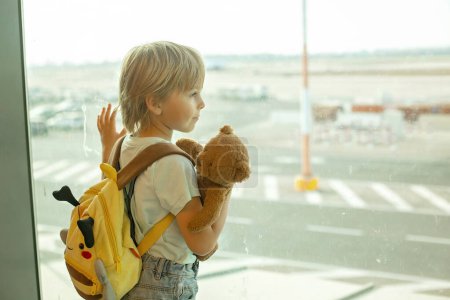 Foto de Niño, mirando desde la ventana del aeropuerto los aviones, despegando y aterrizando mientras espera para abordar el avión para unas vacaciones - Imagen libre de derechos