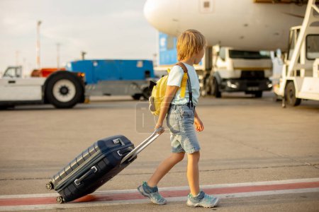 Téléchargez les photos : Mignon enfant blond, enfant avec sac à dos, embarquement à l'aéroport au coucher du soleil, profiter de la vue de l'extérieur - en image libre de droit