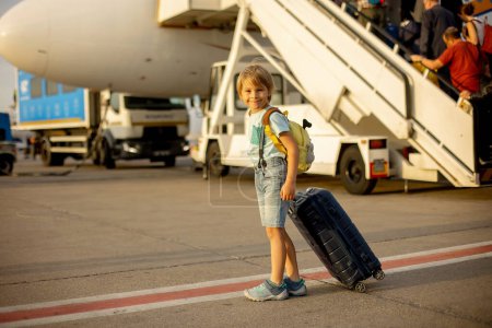 Foto de Niño rubio lindo, niño con mochila, abordar el avión en el aeropuerto al atardecer, disfrutar de la vista desde el exterior - Imagen libre de derechos