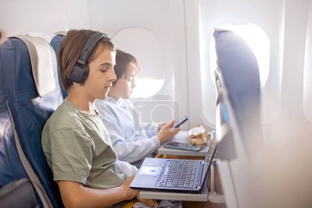 Photo for Cute child, boy, watching TV on board of aircraft, traveling on vacation with parent and siblings going for a summer holiday - Royalty Free Image