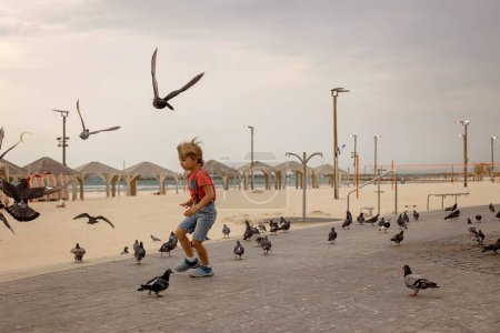 Téléchargez les photos : Enfant, garçon, courir sur la plage de Tel Aviv avec des pigeons le soir, été - en image libre de droit