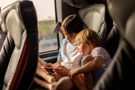 Téléchargez les photos : Enfants, frères et sœurs, jouer sur un téléphone portable pendant un long voyage en bus, vacances en famille - en image libre de droit