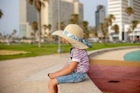 Photo for Cute child with straw hat, enjoying the seaside views in Tel Aviv on a hot summer day, afternoon - Royalty Free Image