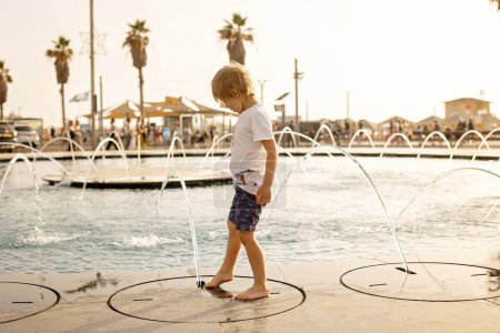 Foto de Lindo niño, niño, jugando con agua en la fuente en Tel Aviv, luces y colores - Imagen libre de derechos