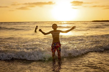 Foto de Adolescentes felices, corriendo y jugando en la playa al atardecer, salpicando agua y saltando sobre la arena. Tel Aviv, Israel - Imagen libre de derechos