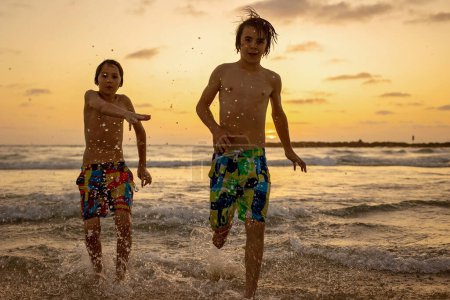 Photo for Happy teenager boys, running and playing on the beach on sunset, splashing water and jumping on the sand. Tel Aviv, Israel - Royalty Free Image