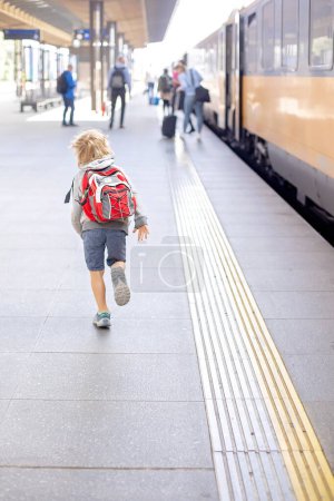 Foto de Lindo niño preescolar con mochila, corriendo para el tren en una estación de tren, verano - Imagen libre de derechos