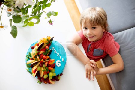 Photo for Cute preschool boy with birthday cake with candles at home, preparing for party with friends and siblings - Royalty Free Image