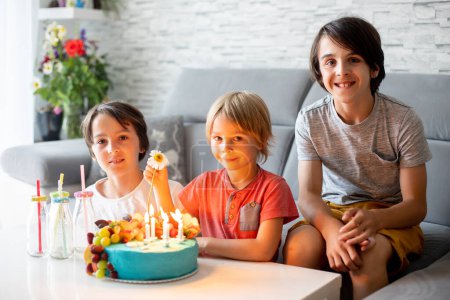 Foto de Lindo niño preescolar con pastel de cumpleaños con velas en casa, preparándose para la fiesta con amigos y hermanos - Imagen libre de derechos
