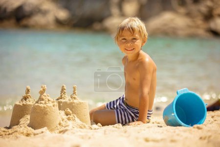 Foto de Niño feliz en la playa, la construcción de castillo de arena, disfrutar del verano, jugar. Chalkidiki, Grecia - Imagen libre de derechos