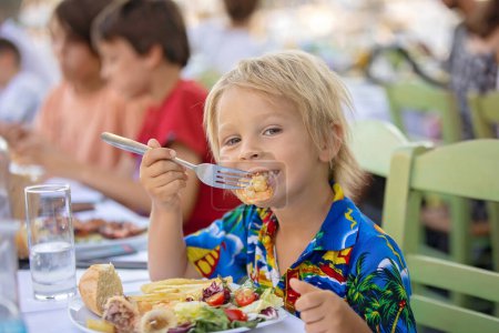 Photo for Sweet child, sitting in restaurant summertime outdoor, eating seafood, shrimps, calamari, octopus and french fries - Royalty Free Image